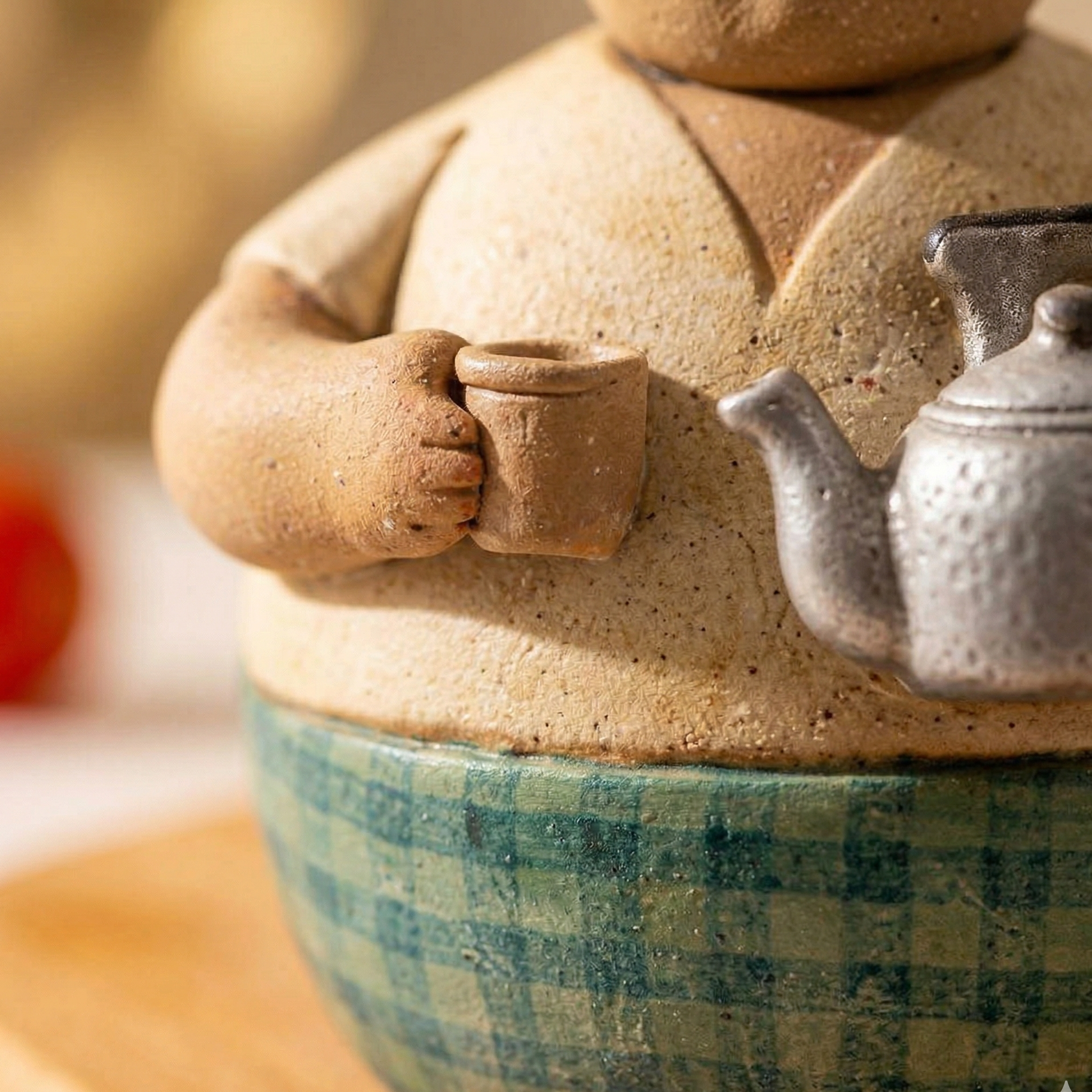 Ceramic teapot with checkered base and small teacup attachment on a wooden surface.