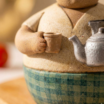 Ceramic teapot with checkered base and small teacup attachment on a wooden surface.