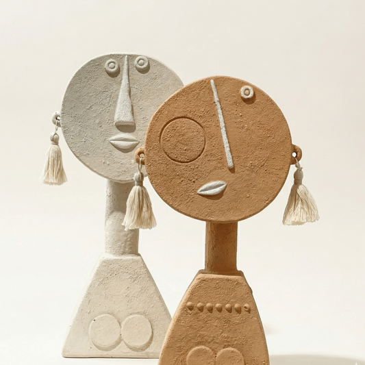 Two ceramic face sculptures with tassels on a light background