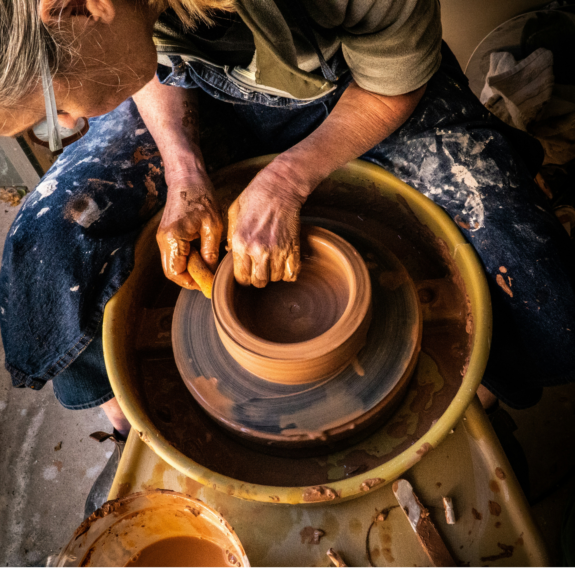 Person working with clay on a pottery wheel in a workshop setting