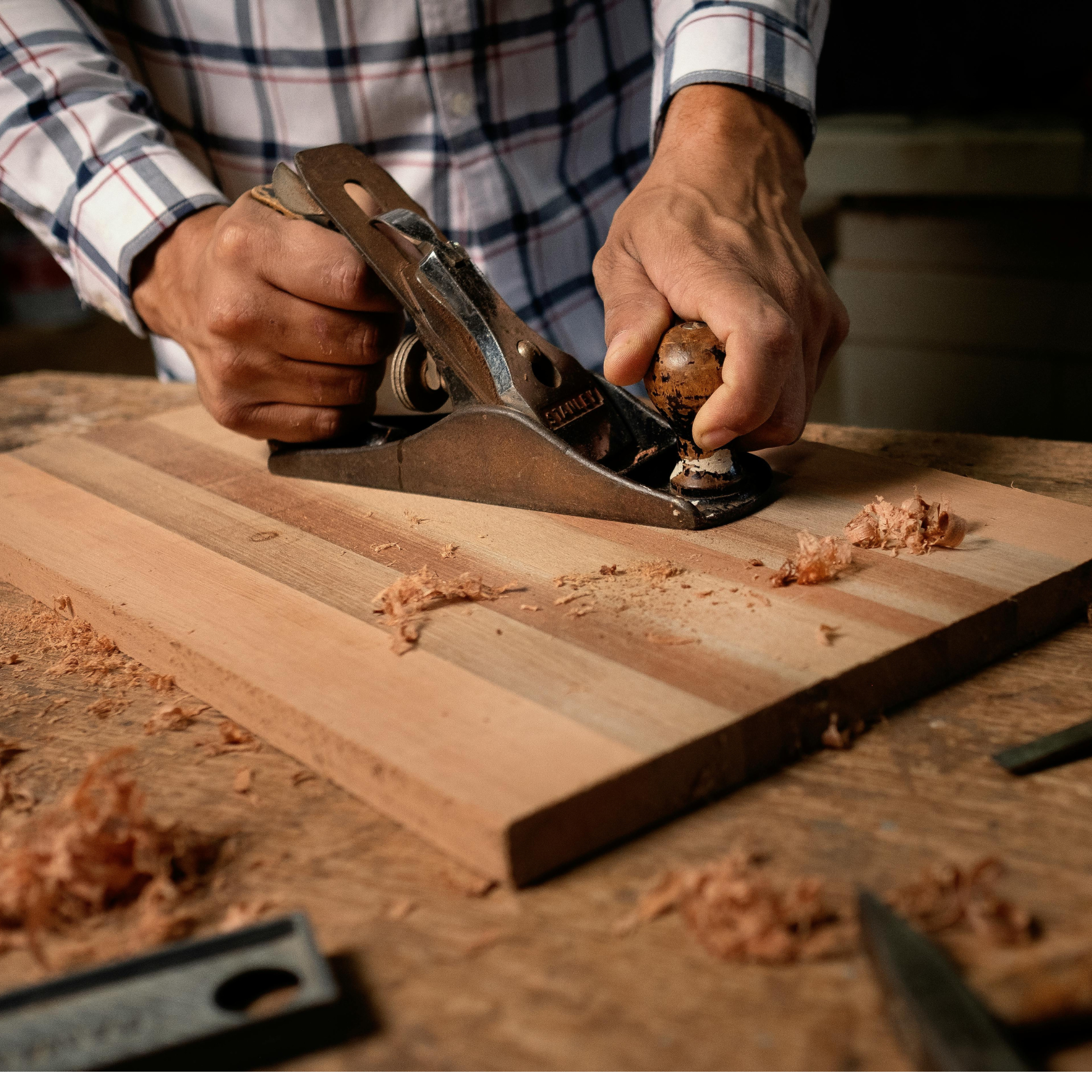 Person using a hand plane on a wooden surface with wood shavings.