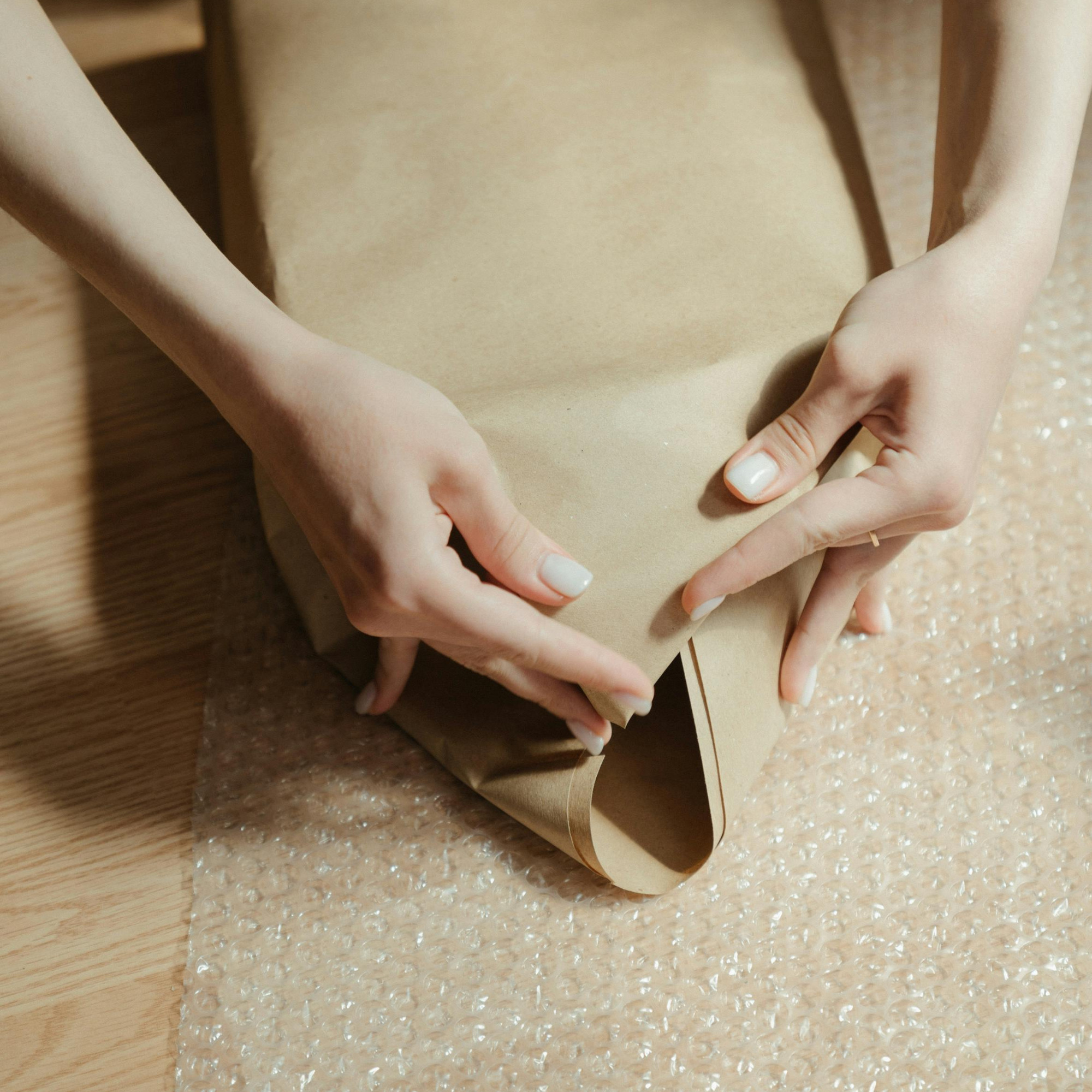 Person wrapping a package with brown paper on a bubble wrap surface