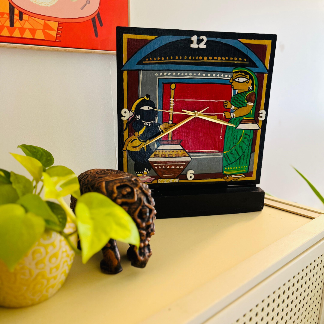 wooden table clock displayed on top of a shelf to showcase a Jamini Roy art featuring krishna and yashoda 